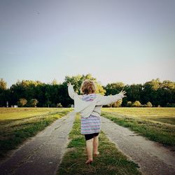 Rear view of girl walking on field against clear sky