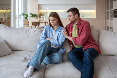 Smiling friends using phone while sitting on sofa at home