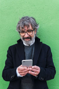 Mature businessman posing isolated over green wall background using mobile phone