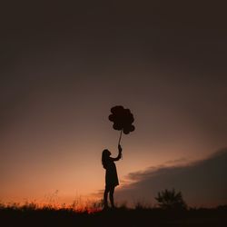 Silhouette of young woman holding balloons