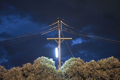 Low angle view of power line against cloudy sky at night