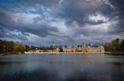 Buildings by lake against cloudy sky