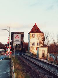 Road sign by railroad tracks against sky