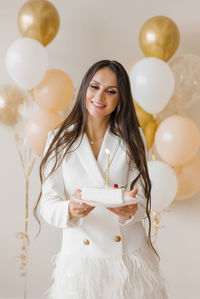 Positive woman celebrating anniversary dressed in stylish feather dress posing with birthday candle