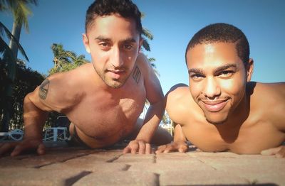 Portrait of smiling shirtless friends lying at poolside