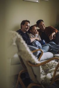 Happy gay couple watching movie with daughter while sitting on sofa at home