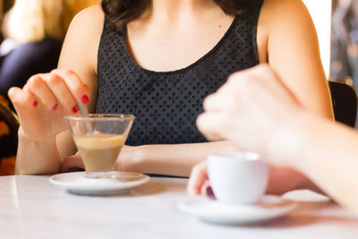 Midsection of woman drinking glass on table