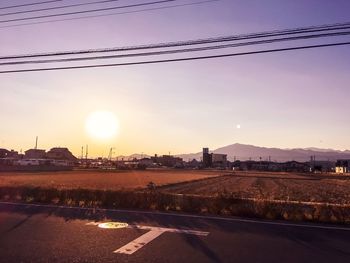 Road by city against sky during sunset