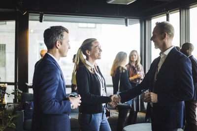 Happy male and female congress shaking hands while standing with colleague in office