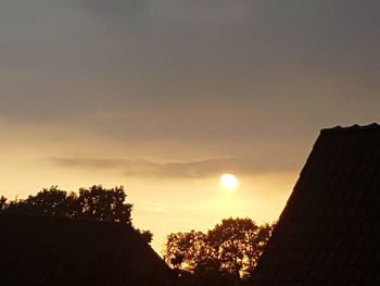 Low angle view of silhouette trees and buildings against sky during sunset