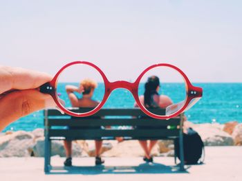 Couple sitting on bench on beach seen through eyeglasses