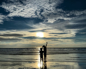 Silhouette man standing on beach against sky during sunset