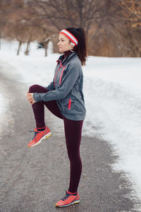 Full length of woman exercising on road during winter
