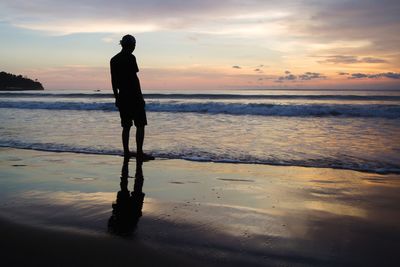 Silhouette man standing on beach against sky during sunset