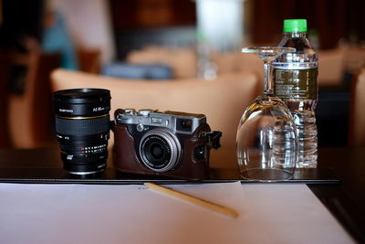 Close-up of camera with lens and water bottle on table