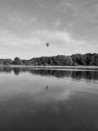 Hot air balloon flying over lake against sky