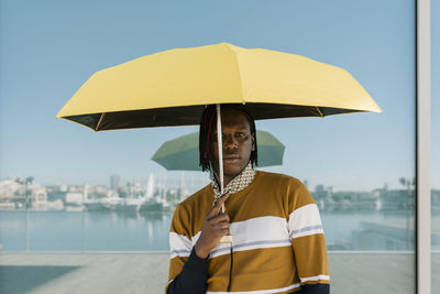 Man holding yellow umbrella while standing against glass wall