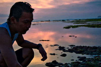 Side view of young man on beach against sky during sunset