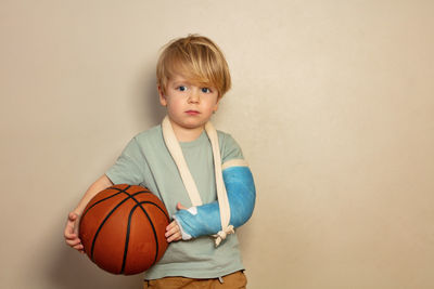 Portrait of boy holding basketball while standing against wall