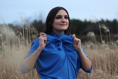 Woman tying bow of top while standing against sky