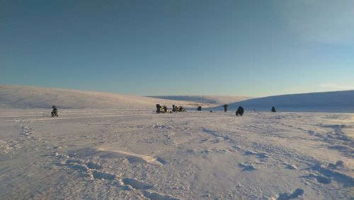 People on snow covered landscape against clear sky