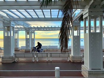 Side view of person riding bicycle on footpath by sea at sunset