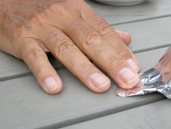 Cropped hand of man holding candy wrapper on wooden table