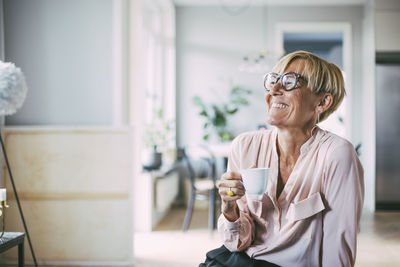 Laughing woman looking to the side having a coffee at home