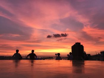 Silhouette people on sea against orange sky