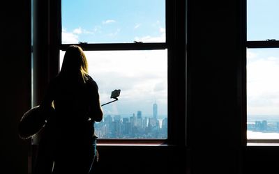 Rear view of silhouette woman looking through window