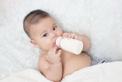 Portrait of cute boy drinking milk from bottle lying on bed