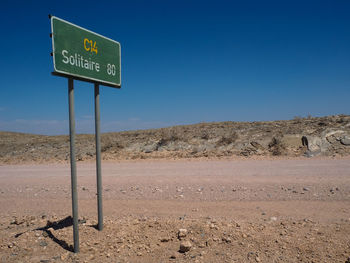Road sign on desert against clear blue sky
