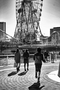 People walking on footpath by ferris wheel against sky