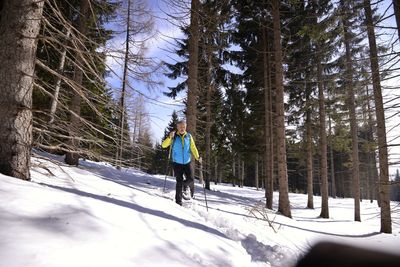 Low angle view of senior man hiking on snow covered field in forest