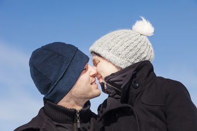 Low angle view of romantic couple kissing against sky during winter