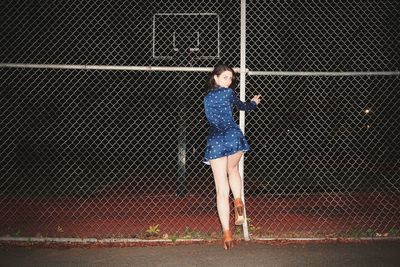 Full length portrait of woman standing by chainlink fence