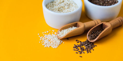 Wooden spoons with sesame and flax seeds lies in a white mortar on a yellow background. healthy 