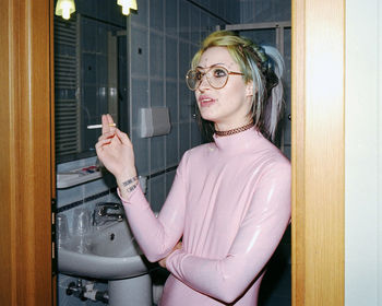 Young woman with freckles and pierced smoking cigarette in bathroom