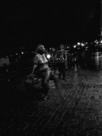 Rear view of woman sitting on street at night