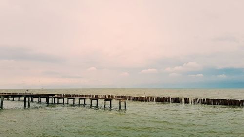 Wooden posts on pier over sea against sky