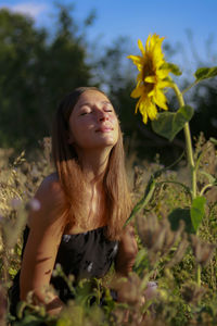Woman with eyes closed sitting by sunflower on field during sunny day