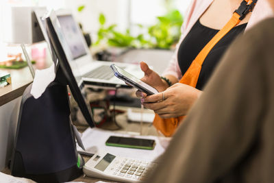 Woman using mobile phone at cashier counter in the cafe, small business owner retail.