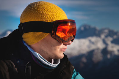 Male skier overlooking snow covered mountains on a sunny day, sun beams reflection in ski goggles