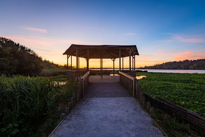 Gazebo on footpath by sea against sky during sunset