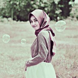 Rear view of woman with bubbles standing on field