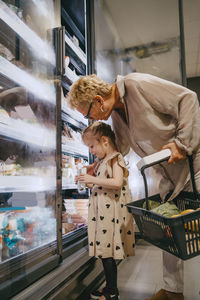 Senior woman with granddaughter choosing frozen food while doing shopping at grocery store