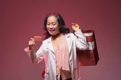 Portrait of young woman holding shopping bags while standing against yellow background