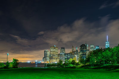 Grassy field against illuminated buildings and sky in park at night