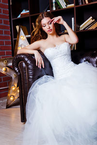 Bride wearing wedding dress sitting on sofa at home