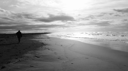 Rear view of woman walking on beach against sky